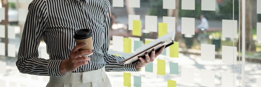 Close up business woman reading a book and writing notes while standing near window