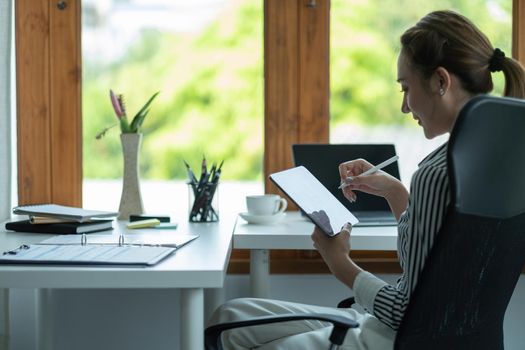 Attractive business asian woman using a digital tablet while sitting in workplace desk in an office