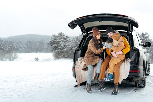 Winter portrait of a family sit on car trunk enjoy their vacation in snowy forest