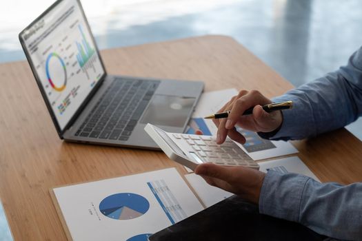 Close up of businessman or accountant hand holding pen working on calculator to calculate business data, accountancy document and laptop computer at office, business concept.