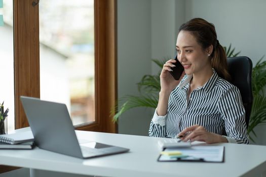 Young accountant hand holding smartphone to call marketing consultants and using laptop computer to analyze sales growth in the global workplace market. accounting concept.