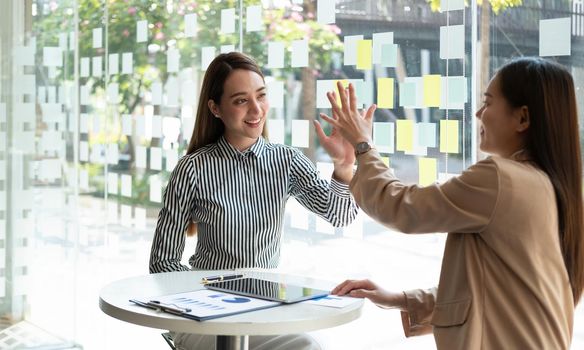 Asian businesswoman giving high five to colleague in meeting. Happy business professionals having meeting in office conference room