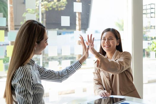 Asian businesswoman giving high five to colleague in meeting. Happy business professionals having meeting in office conference room