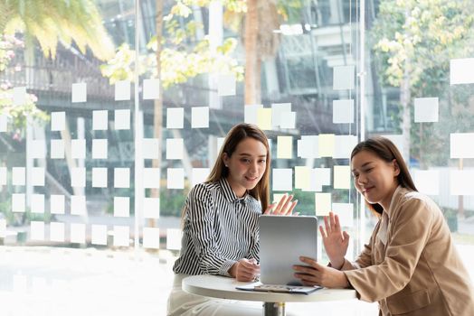 Two asia businesswoman using digital tablet talk to colleagues about plan in video call while smart working from home at living room. Self-isolation, social distancing, quarantine for corona virus prevention.