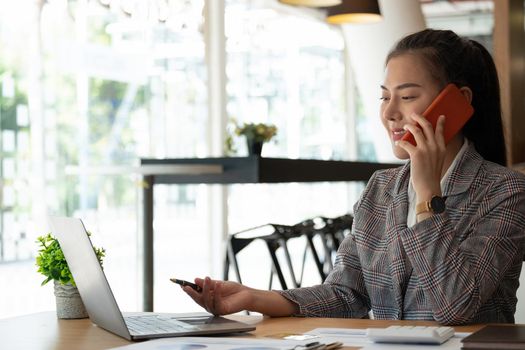 Young accountant hand holding smartphone to call marketing consultants and using laptop computer to analyze sales growth in the global workplace market. accounting concept.