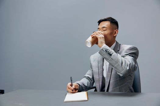 man writes in a notebook sits on the table with coffee official Gray background. High quality photo