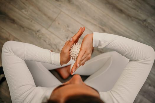 Athletic slim caucasian woman doing thigh self-massage with a massage ball indoors. Self-isolating massage.