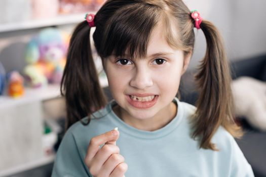 Dental medicine or temporary teeth health care concept. Portrait of a baby girl with a toothless smile. Shows a ripped tooth into the camera in an extended hand. Shift focus from tooth to face.