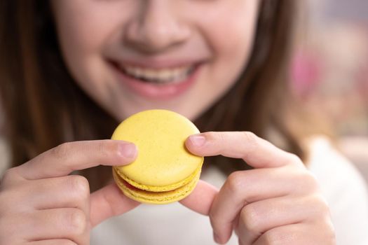 Close up front view unrecognizable brunette kid girl bites yellow macaron cookie. Tasty sweet color macaron. Traditional French multicolored macaroon. Food concept.