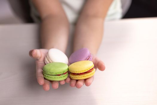 Children's hands hold macarons on a white background. Traditional French multicolored macaroon. Food concept.