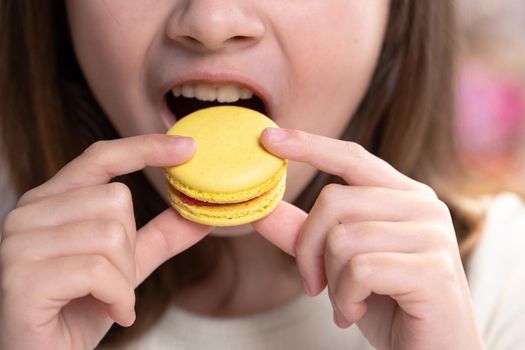 Close up of gorgeous school girl biting french macaroon, enjoying eating, confectionary desire and pleasure. Attractive brunette female girl on home background, licks her lips, eating macaron.