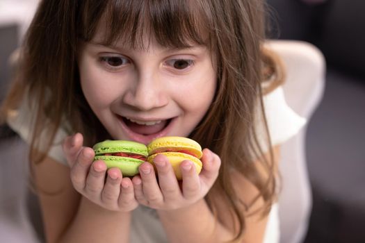 Attractive smiling cute school kid girl holds four tasty cookies in her hands. Traditional French multicolored macaroon. Food concept.