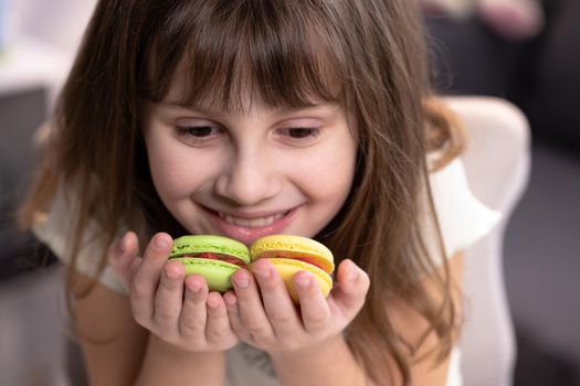 Smiling cute school kid girl holds four tasty cookies in her hands. Traditional French multicolored macaroon. Food concept.