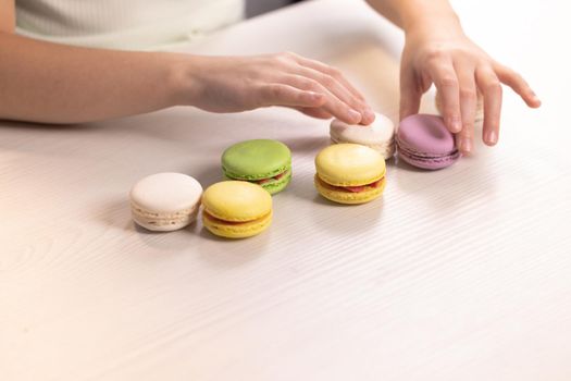 Happy little girl plays with dessert macarons on home background. Kid girl plays macarons cookie. Dessert person, sweet tooth, gourmet.