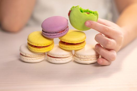 Delicious multi-colored cookies in the hands of a child. Macaron. Kid girl bites pistachio green macaron cookie. Dessert person, sweet tooth, gourmet.