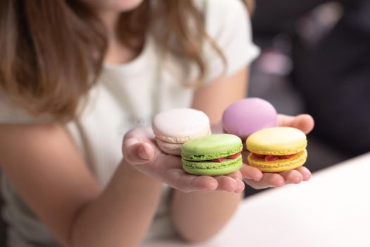 Child's hands taking French macarons of colorful macarons isolated on white table. Kid girl plays macarons cookie. Dessert person, sweet tooth, gourmet.