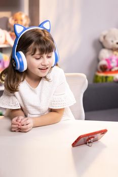 Cute small kid girl vlogger talking to camera at home recording vlog for social media blog, video conference calling virtual friend having online meeting sitting in chair.