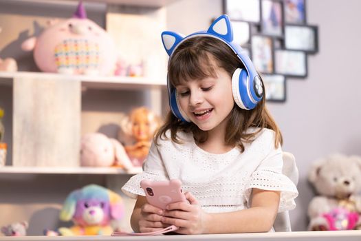 Happy caucasian little teen girl holding cell phone using smartphone device at home. Smiling young woman blogger subscribing new social media, buying in internet, ordering products online in apps.