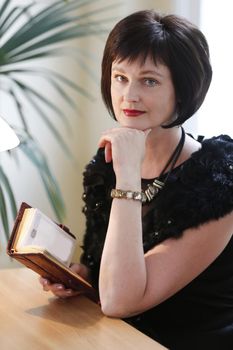 Portrait of a middle-aged woman with a book. An adult brunette woman looks at the camera.