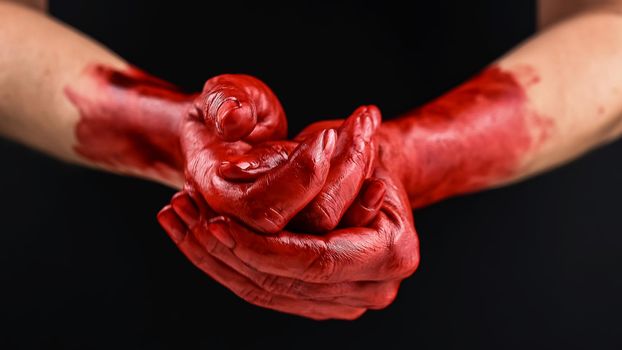 Woman holding blood-stained palms together on black background