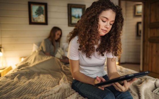Two beautiful women lying in bed, holding and watching laptop