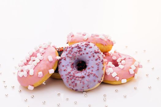 Assortment of donuts of different flavors. Chocolate frosted, pink glazed and sprinkles donuts. Donuts with different fillings on the white table.