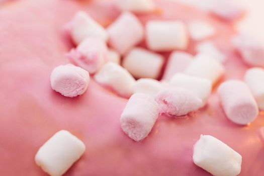 Close up pink and white mini marshmallows on pink donut food light sweet dessert candy delicious sugar. Appetizing sweet donut dessert in pink glaze close-up.