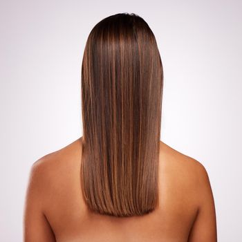 Studio shot of an unrecognizable young woman standing with her back facing the camera to show off her hair against a grey background.