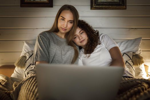 Two beautiful women lying in bed and watching movies on laptop at home
