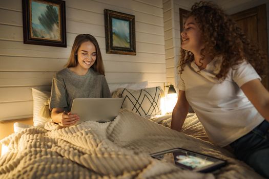Two beautiful women lying in bed, holding and watching laptop
