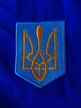 Embroidered Ukrainian trident with yellow threads on a blue background.
