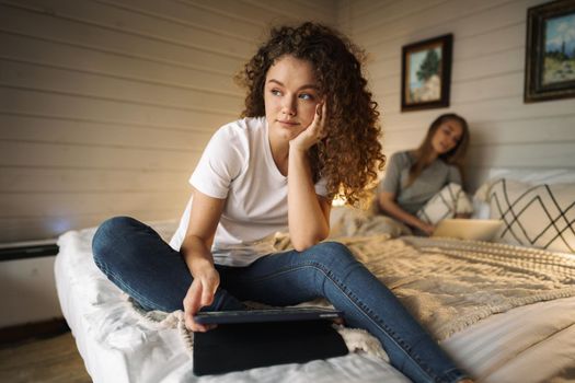 Two beautiful women lying in bed, holding a laptop