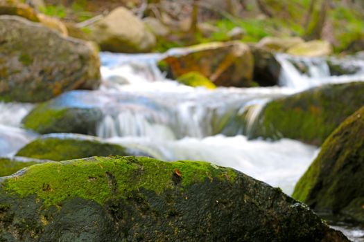 Selective focus. View of the stone with moss. The river flows over rocks