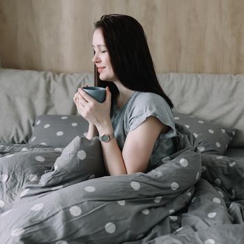 Woman get up and drinking coffee in a cozy bed room at home, early out morning and wake up rest sunny day. Morning quiet time. A young woman enjoing in bed, lazy day, cozy home atmosphere.