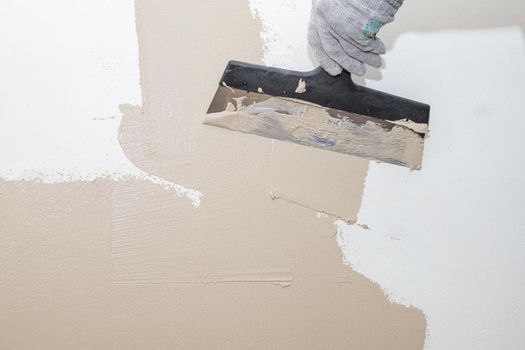 Man plastering wall with putty-knife. Fixing wall surface and preparation for painting.