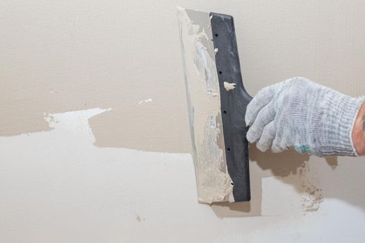 Man plastering wall with putty-knife. Fixing wall surface and preparation for painting.