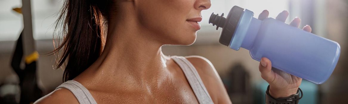 Portrait of lady with sweat on skin in white top holding a water bottle at gym