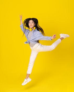 Young happy girl jump on yellow background. Asian young woman with long hair fly in balley style. High quality photo