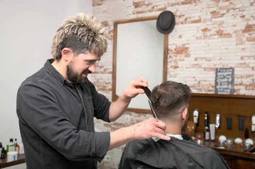 Barber cutting hair with scissors to a handsome young man . High quality photography