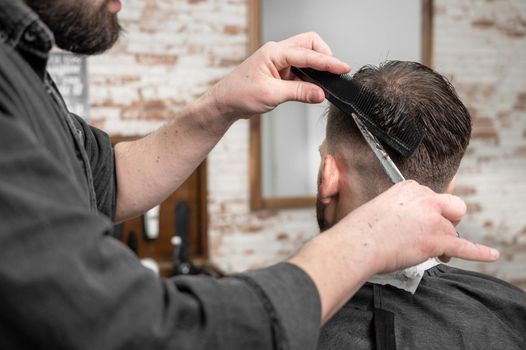 Barber cutting hair with scissors to a handsome young man . High quality photography