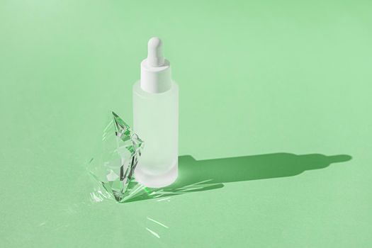 Serum skincare product with collagen and peptide in white bottle with dropper on green backdrop with crystal glass prism refracting light effects and rays of light. Product mockup packaging, banner