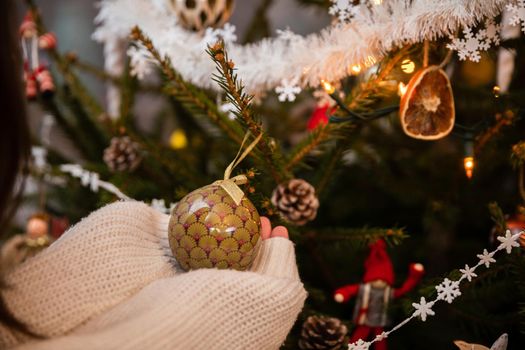 Long sleeves in cream sweater. Christmas tree bauble in delicate feminine hands. An annual Christmas decorating ritual in Poland.