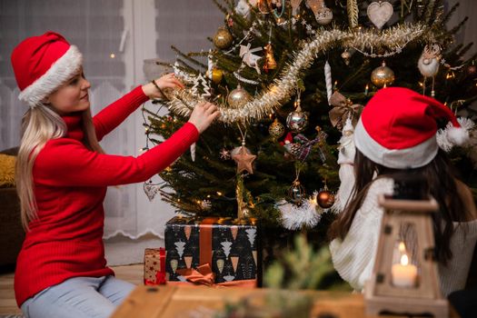 Mother and daughter decorate a live Christmas tree in the living room for Christmas. An annual important Christmas ritual in Poland.