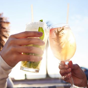 Shot of two female friends celebrating with drinks at a bar outside.