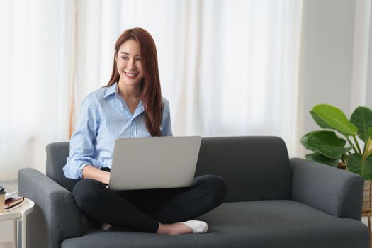 Woman enjoy with content streaming movies or social media application on laptop computer sitting on sofa at home