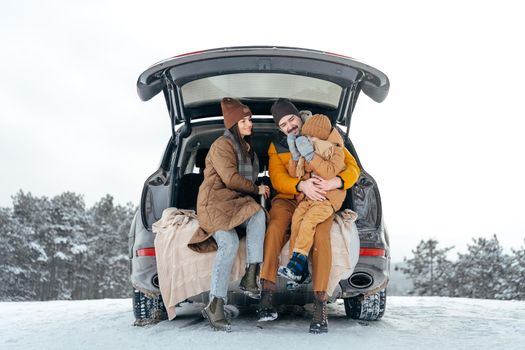Winter portrait of a family sit on car trunk enjoy their vacation in snowy forest
