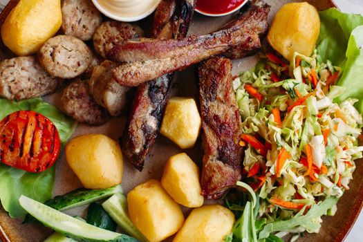 Colorful top view of tasty restaurant meal. clay plate including sausages, cucmbers, boiled potatoes, grilled chicken legs, roasted onion, vegetable salad served with ketchup and mayo.