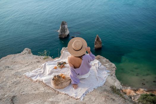 Street photo of a beautiful woman with dark hair in white shorts and a purple sweater having a picnic on a hill overlooking the sea.