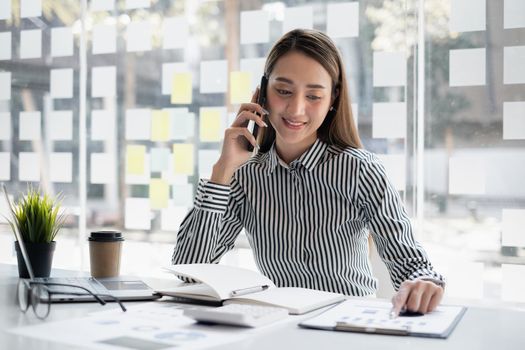 Business woman discuss with partners talking by cell phone. Female technical support agent trying to explain something to a client while working on laptop at call center