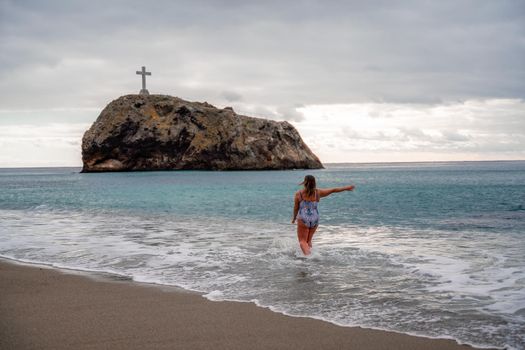 A plump woman in a bathing suit enters the water during the surf. Alone on the beach, Gray sky in the clouds, swimming in winter